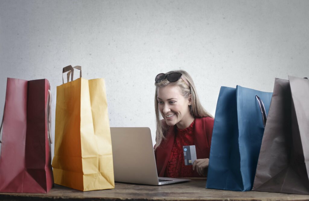 Frau am Laptop mit Kreditkarte in der Hand und Einkaufstaschen auf dem Tisch