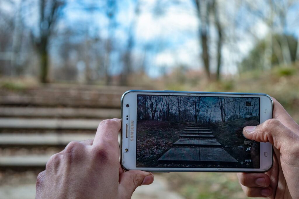 Mann hält Smartphone, auf dessen Bildschirm ein Park zu sehen ist, in dem der Mann steht